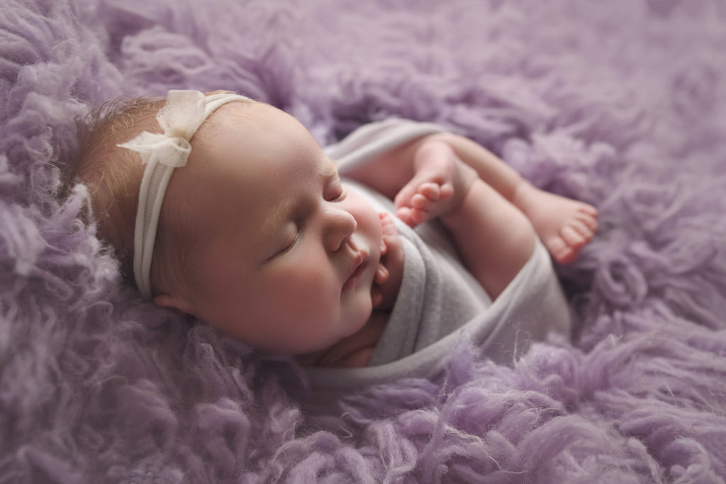 Newborn baby girl in purple fur and a purple wrap