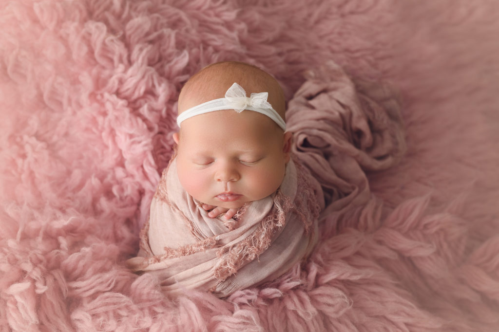 Newborn Baby Girl wrapped in pink scarf on pink fur