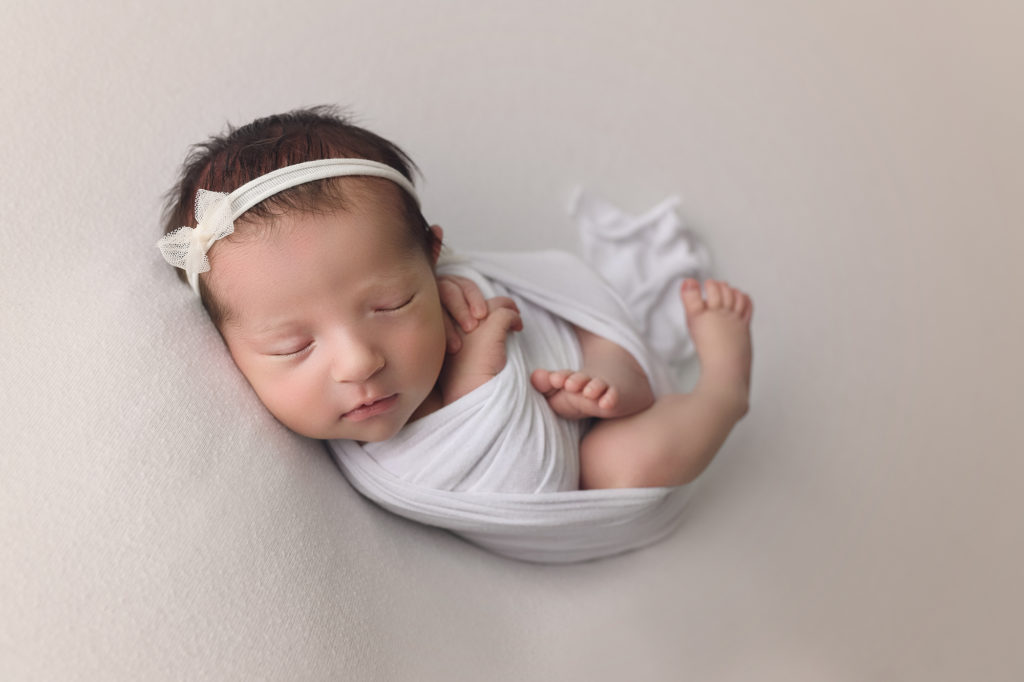 Newborn baby girl in white wrap and matching bow