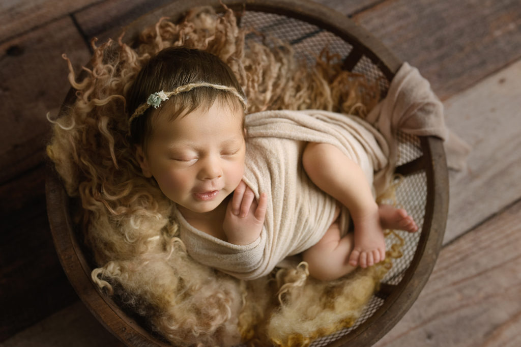 Newborn baby girl in a brown bow with neutral wrap and fur smiling
