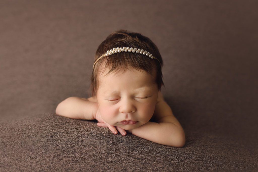 Newborn Baby Girl wearing a pearl headband face forward on a brown blanket