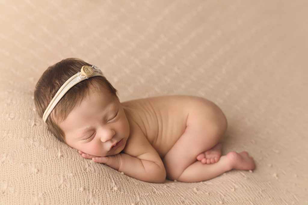 Newborn baby girl on a beaded beige blanket sleeping peacefully