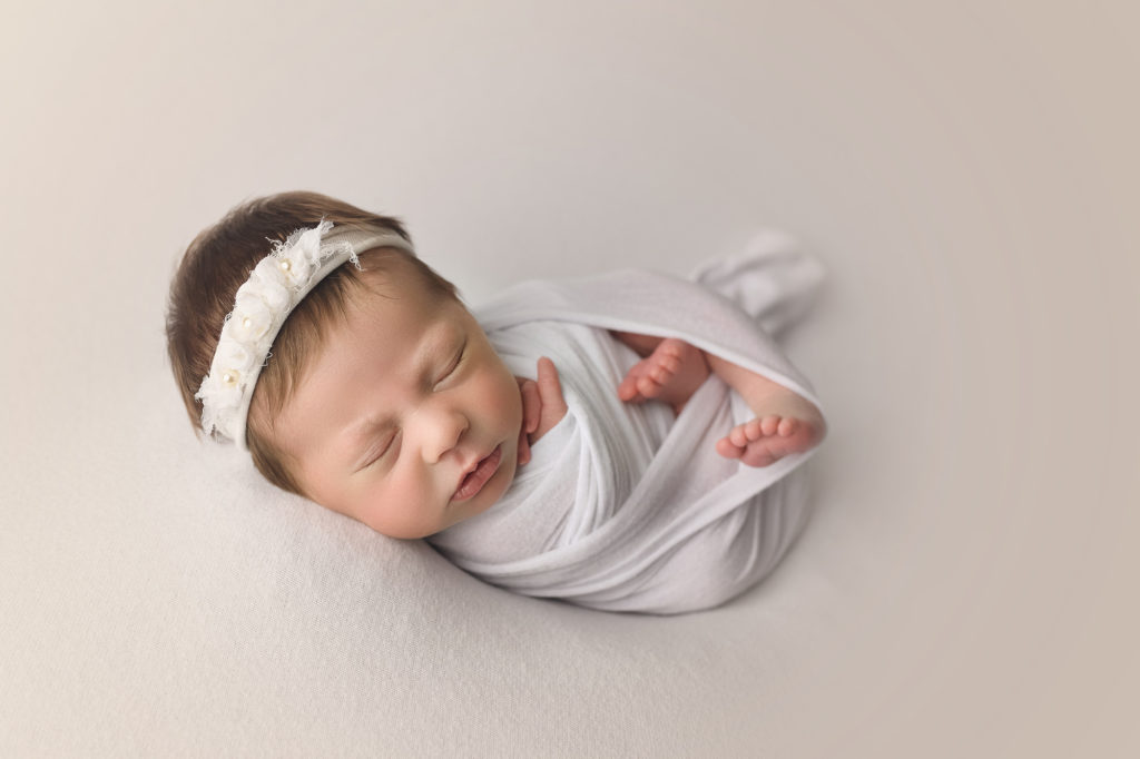 Newborn baby Girl wrapped in white with a white headband