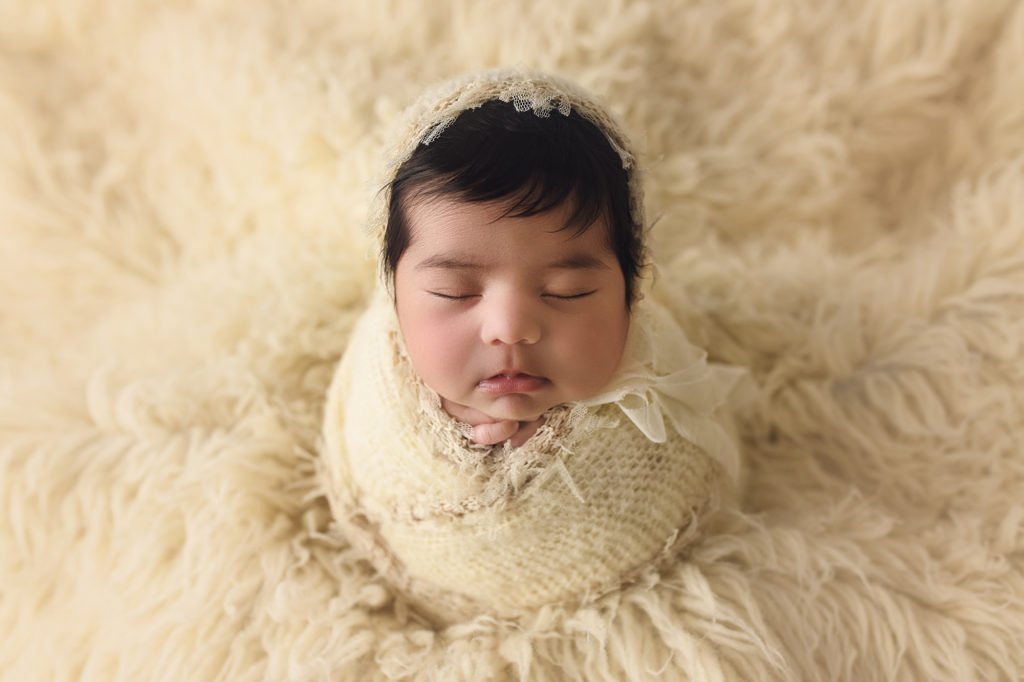 newborn baby girl in potato pose on cream fur with bonnet