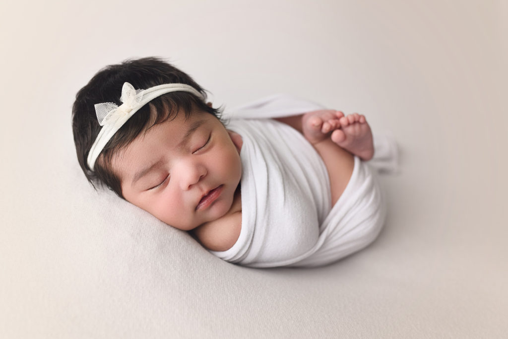 newborn baby girl wrapped in white with white bow