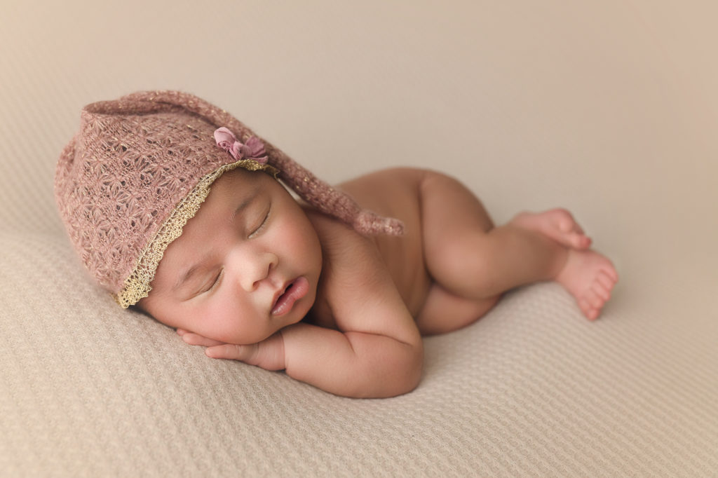 newborn baby girl laying down with pink sleepy hat