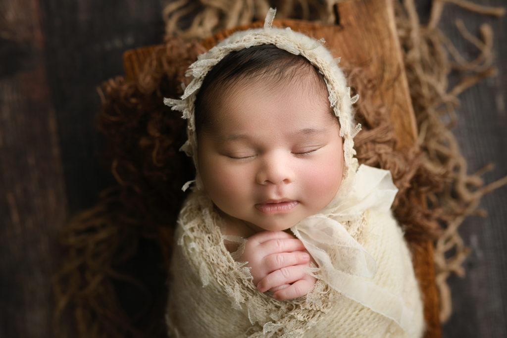 newborn baby girl in basket and white bonnet