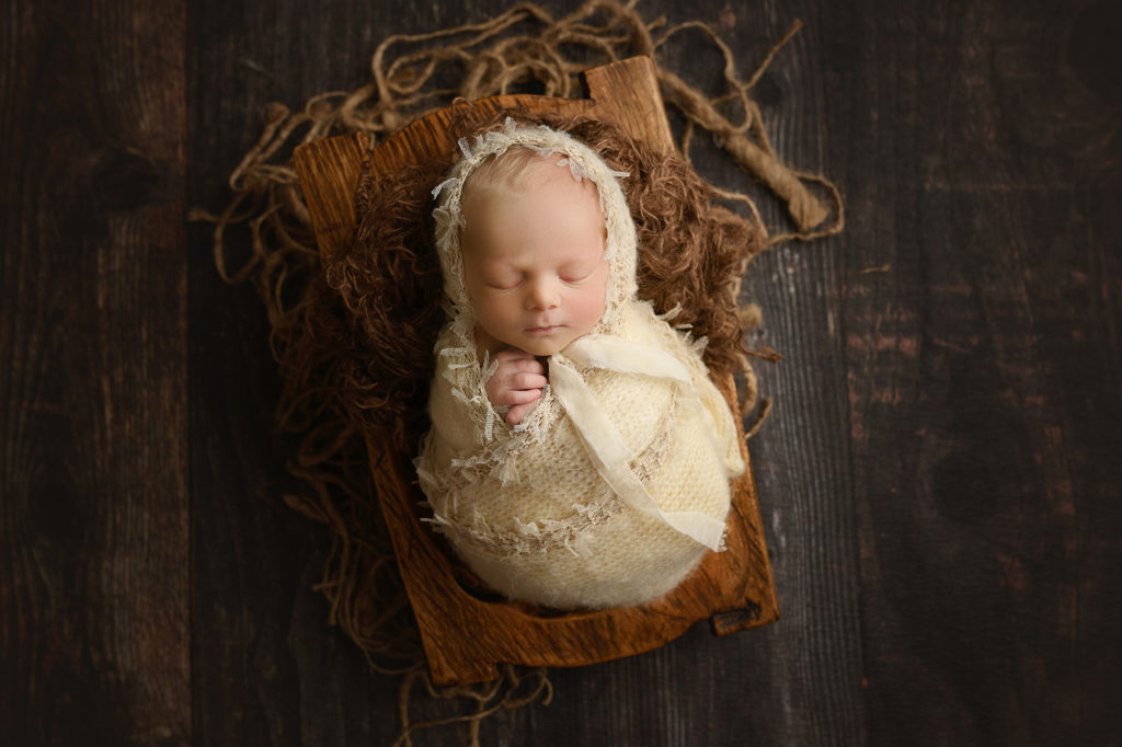 newborn baby girl in bowl wrapped in cream with cream lace bonnet