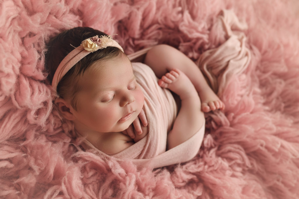 Newborn baby girl on pink fur curled up