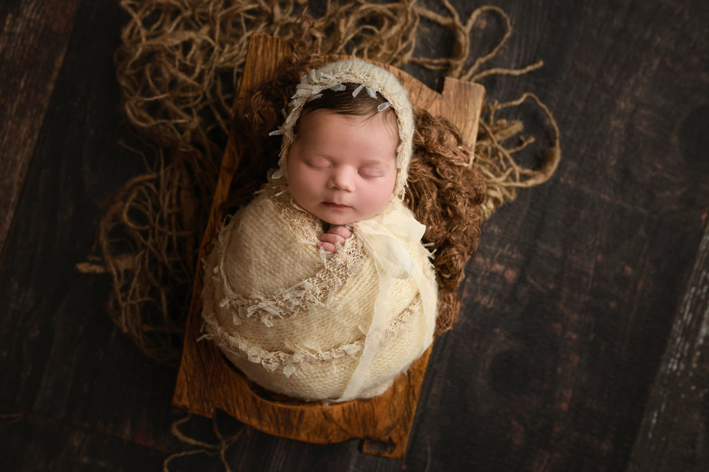 newborn baby girl wrapped in frayed cream wrap and matching bonnet