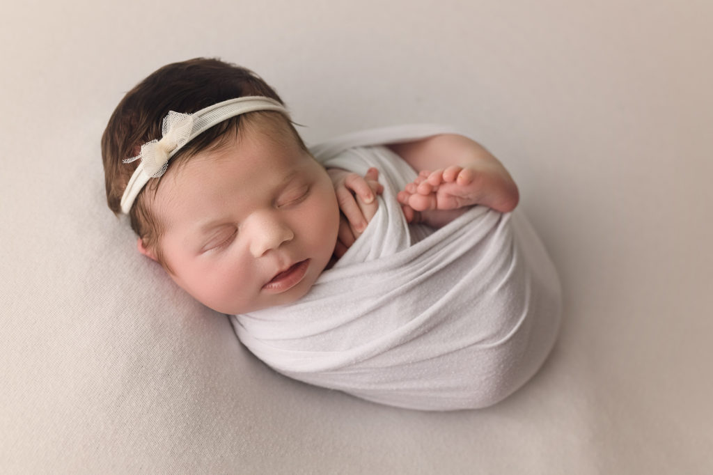 Newborn baby girl wrapped in white with white bow headband