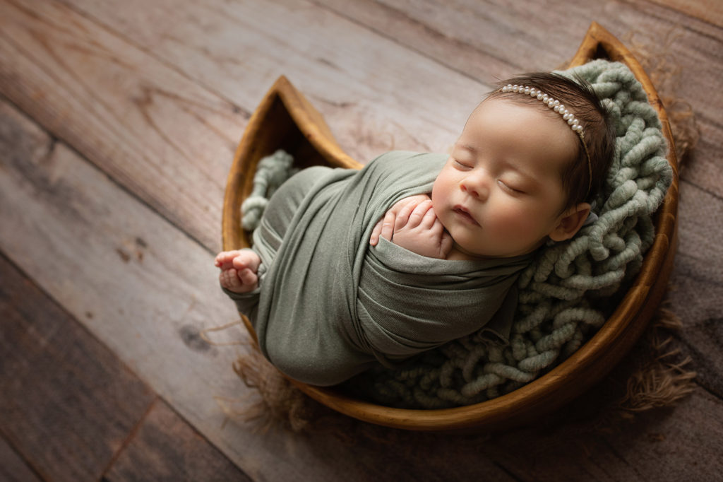 Newborn baby girl wearing pearl headband wrapped in mint and laying on the moon