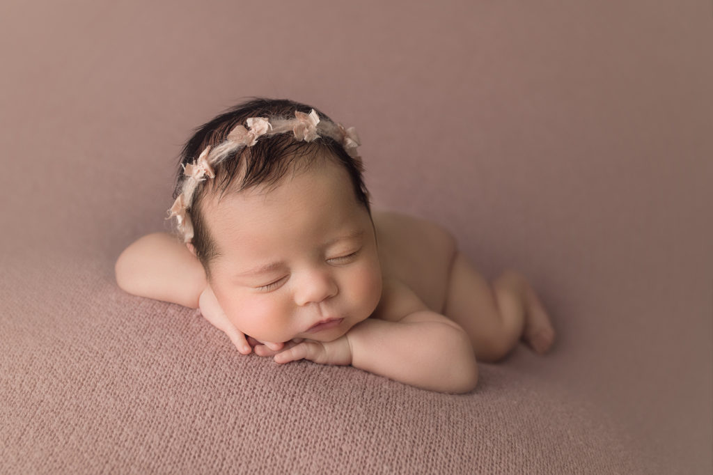 newborn baby girl face forward laying on pink blanket