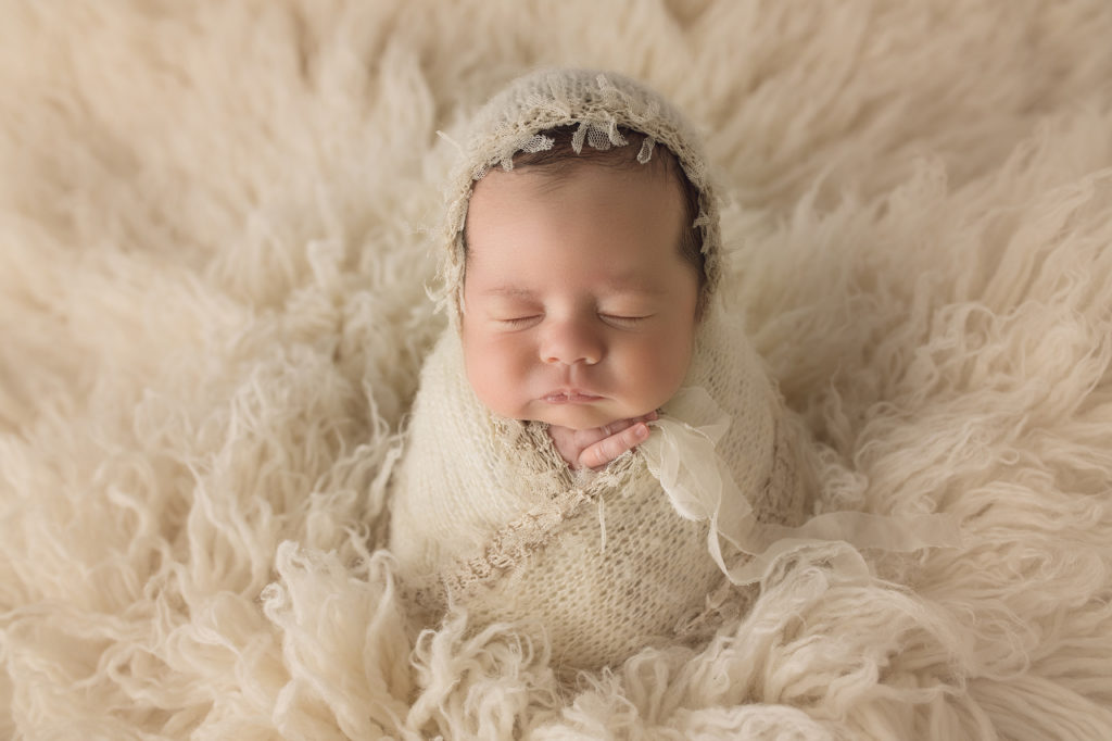 Newborn baby girl laying on snow white fur in Potato Pose