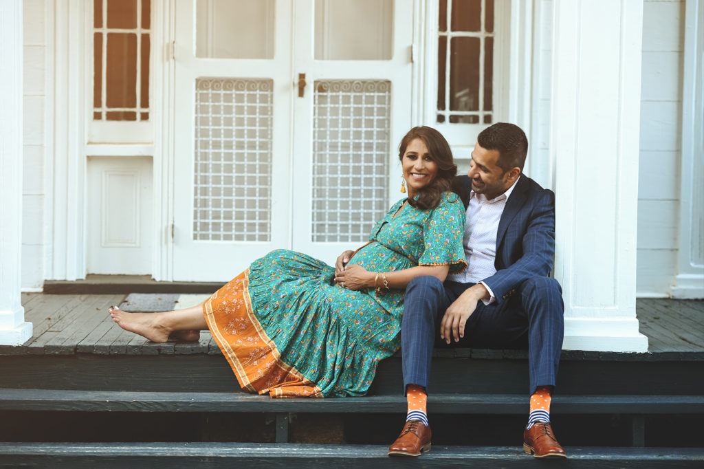 Pregnant mom and soon to be dad sitting on steps to a white house