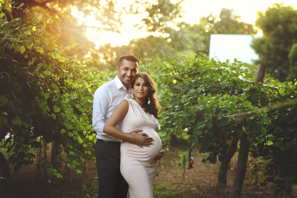 Pregnant mom and soon to be dad standing grape vine beautiful sunset