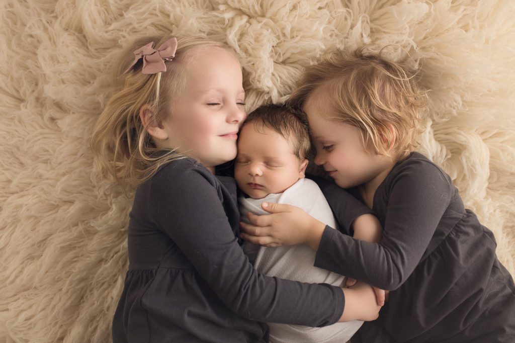 newborn baby boy being hugged by older sisters