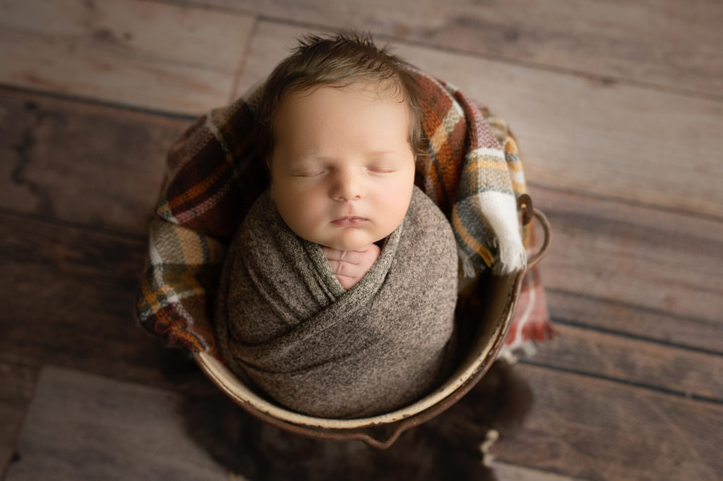 newborn baby boy in cream bucket and plaid brown blanket