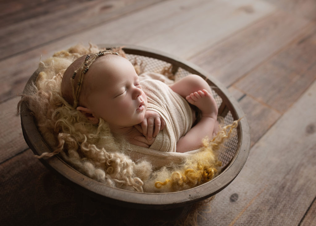 newborn baby girl in round mesh bowl and tan fur