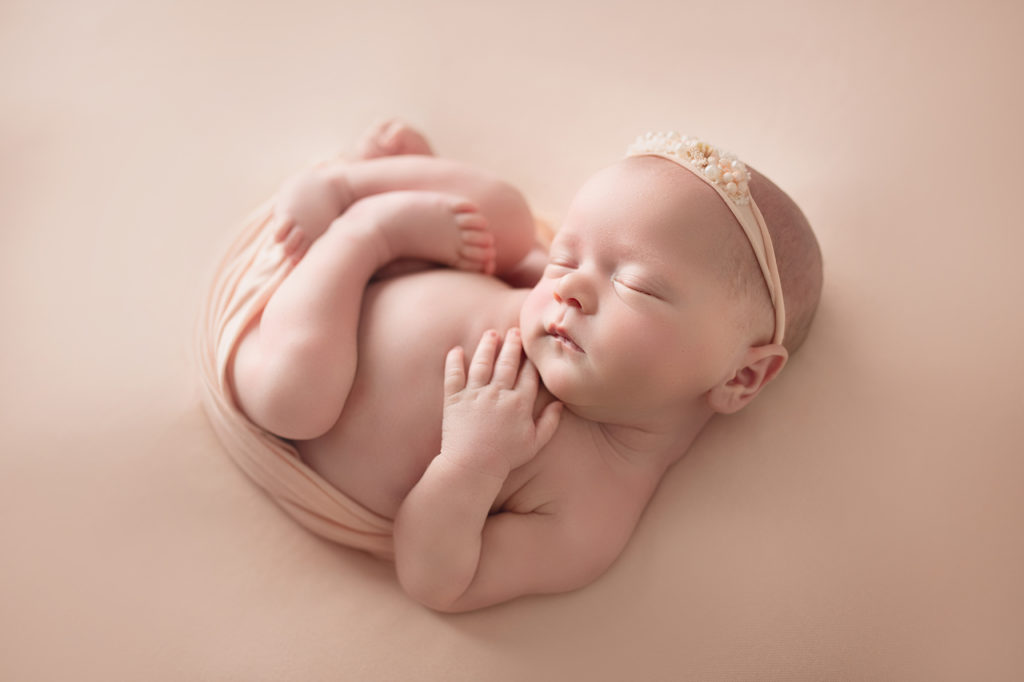 newborn baby girl curled up in pink
