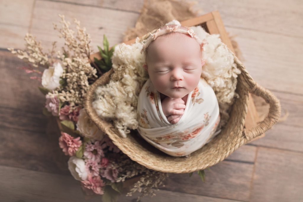 Newborn baby girl in basket in box surrounded by flower