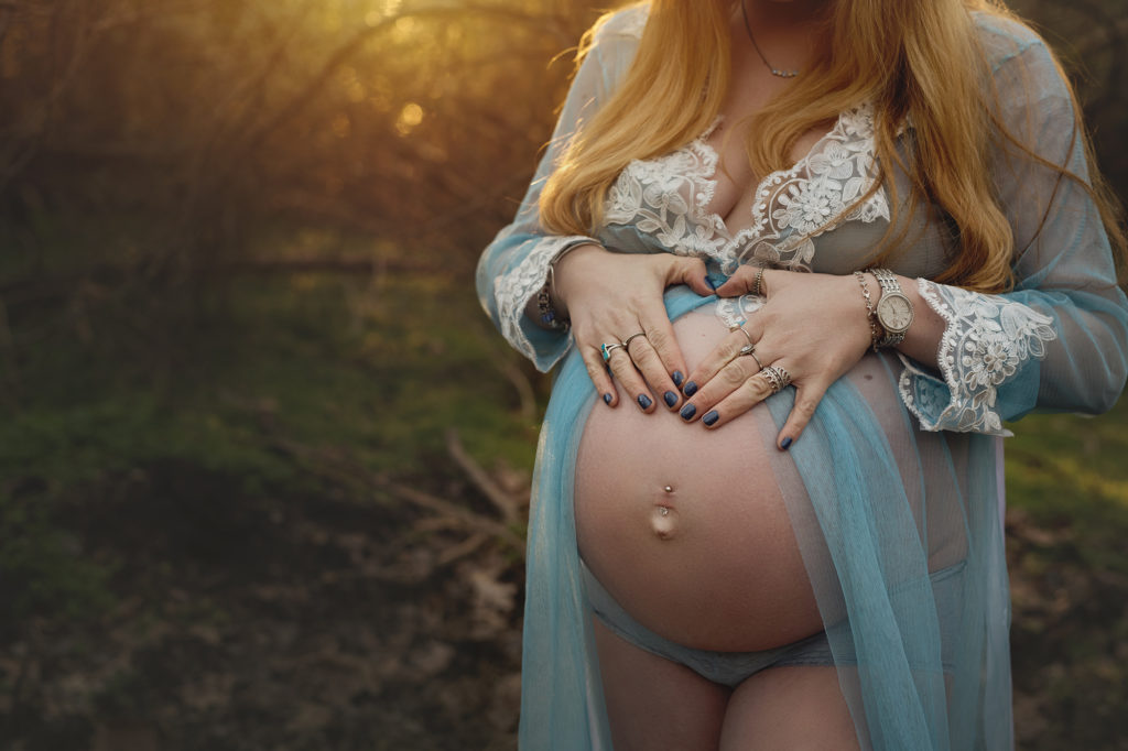 Pregnant Mama wearing sheer blue gown with sunset behind tree