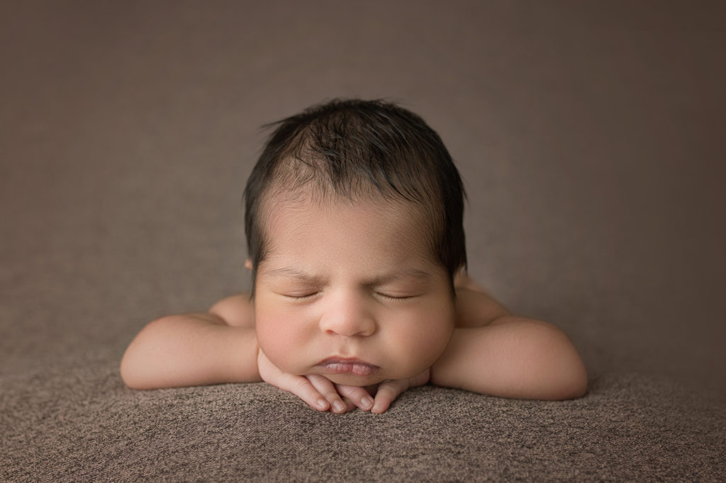 newborn baby boy face on hands sleeping on brown blanket