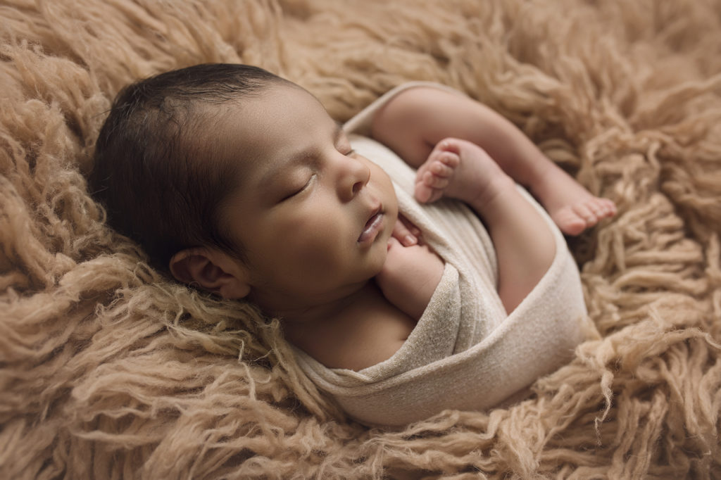 newborn baby boy wrapped in beige on tan fur