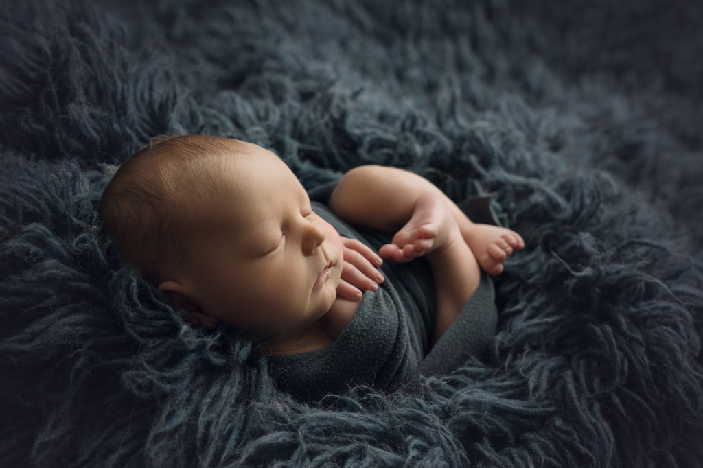 newborn baby boy wrapped in navy blue wrap and laying on navy fur