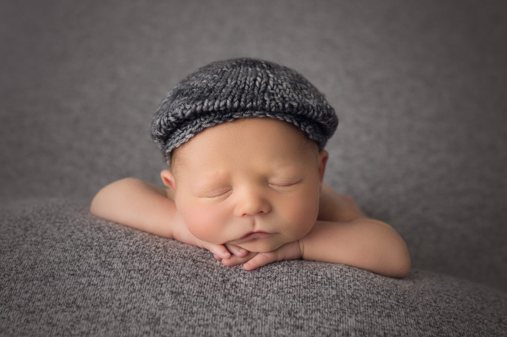 newborn baby boy on gray blanket wearing gray driving hat