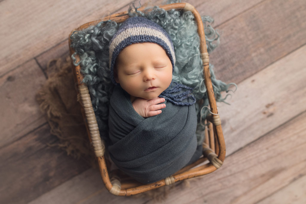 newborn baby boy wrapped in blue and matching blue hat in bamboo basket