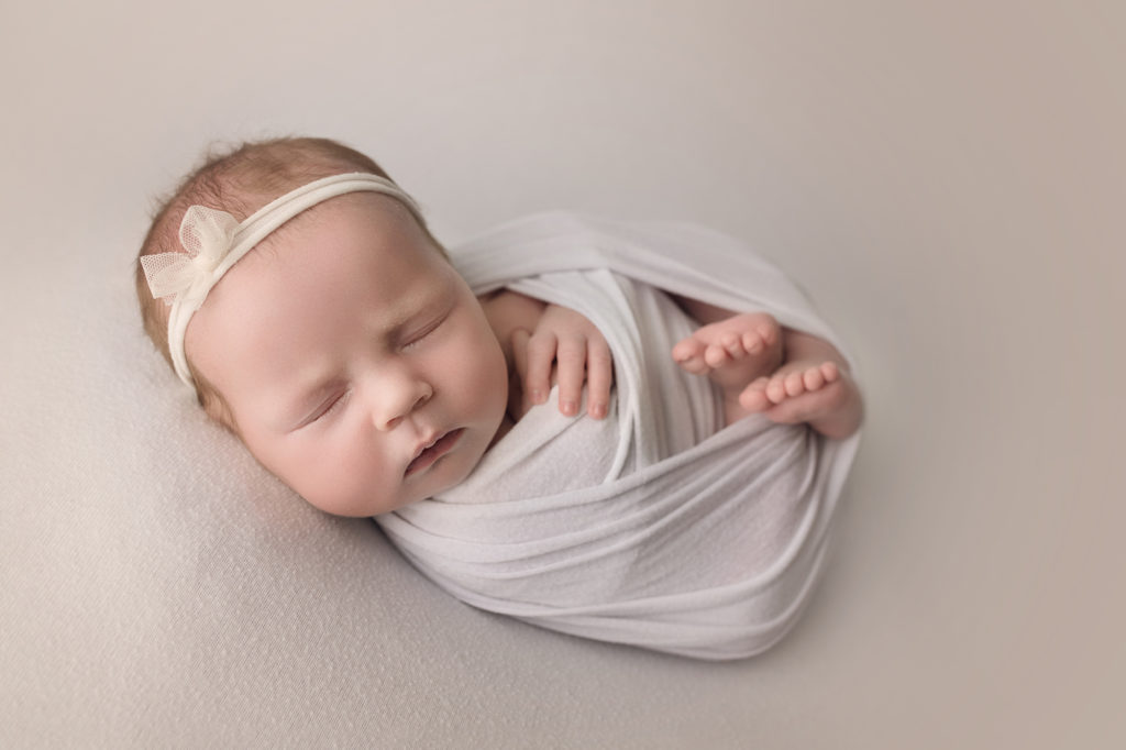 newborn baby girl wrapped in white with matching headband