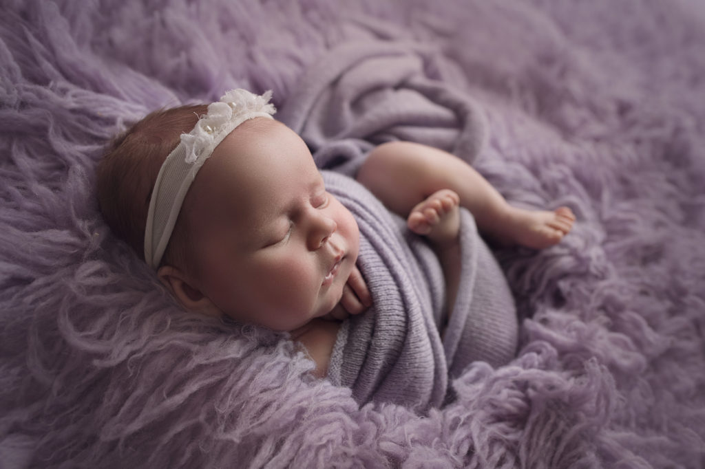 newborn baby girl wrapped in purple curled up in a purple rug