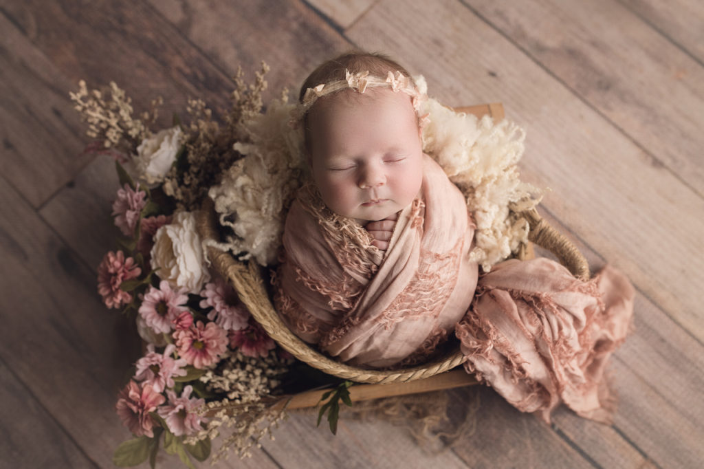 newborn baby girl wrapped in fringe blush wrap surrounded by flowers