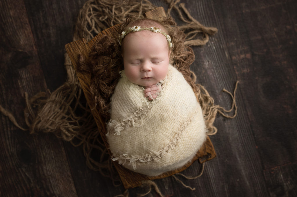 newborn baby girl in cream ruffled wrap in brown rustic bowl