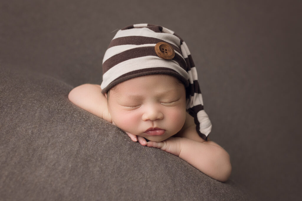 Newborn Boy on Brown Blanket with striped sleeper cap face forward