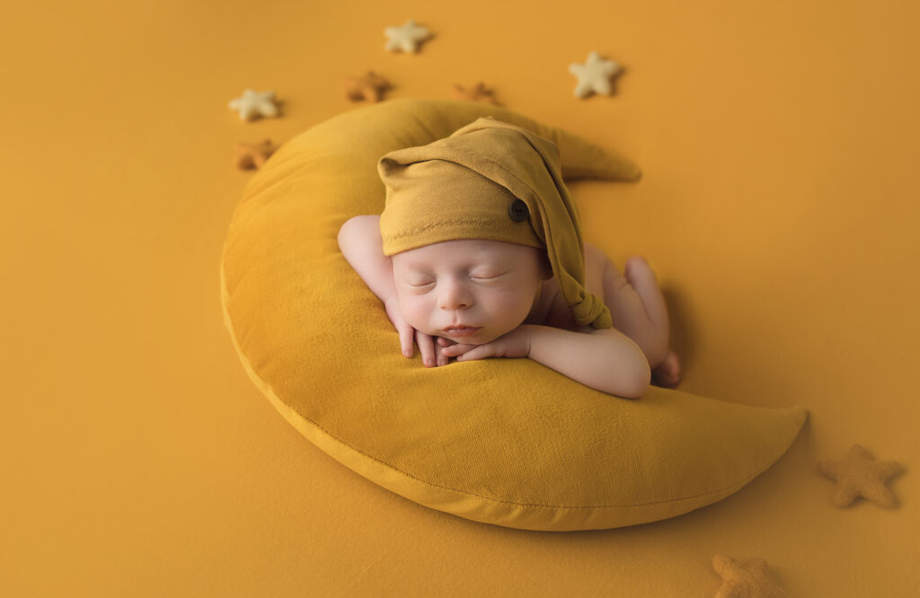 Newborn baby with yellow hat laying on the moon