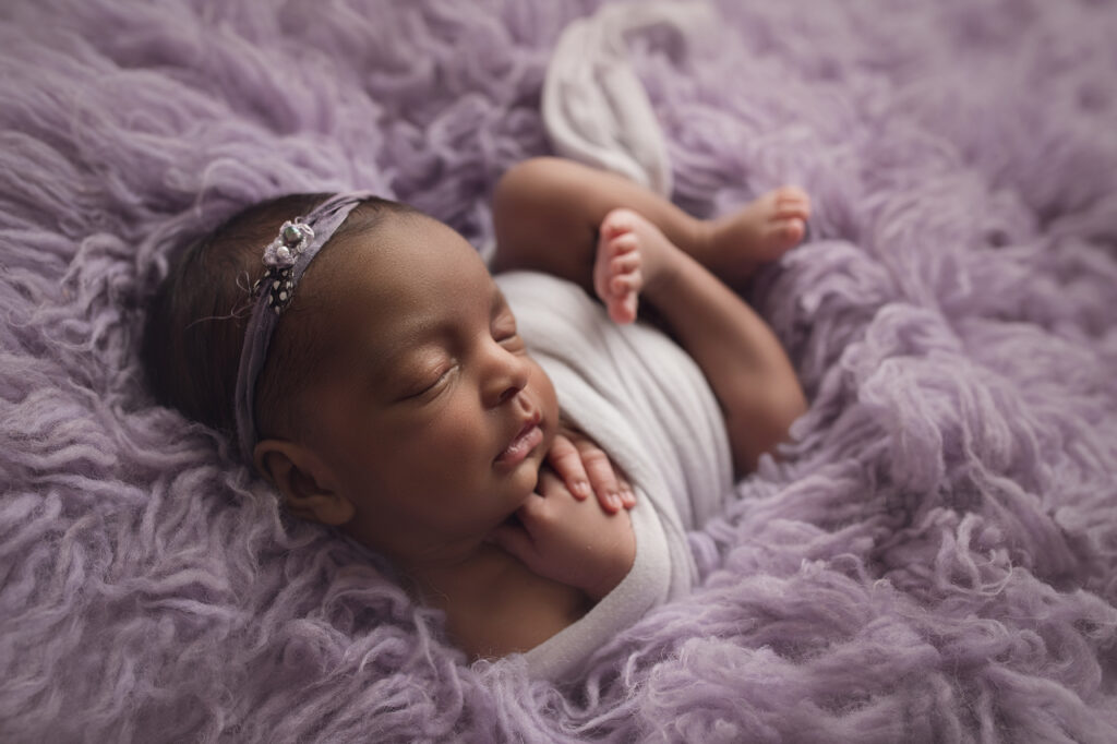 newborn triplet girl laying wrapped up in purple fur