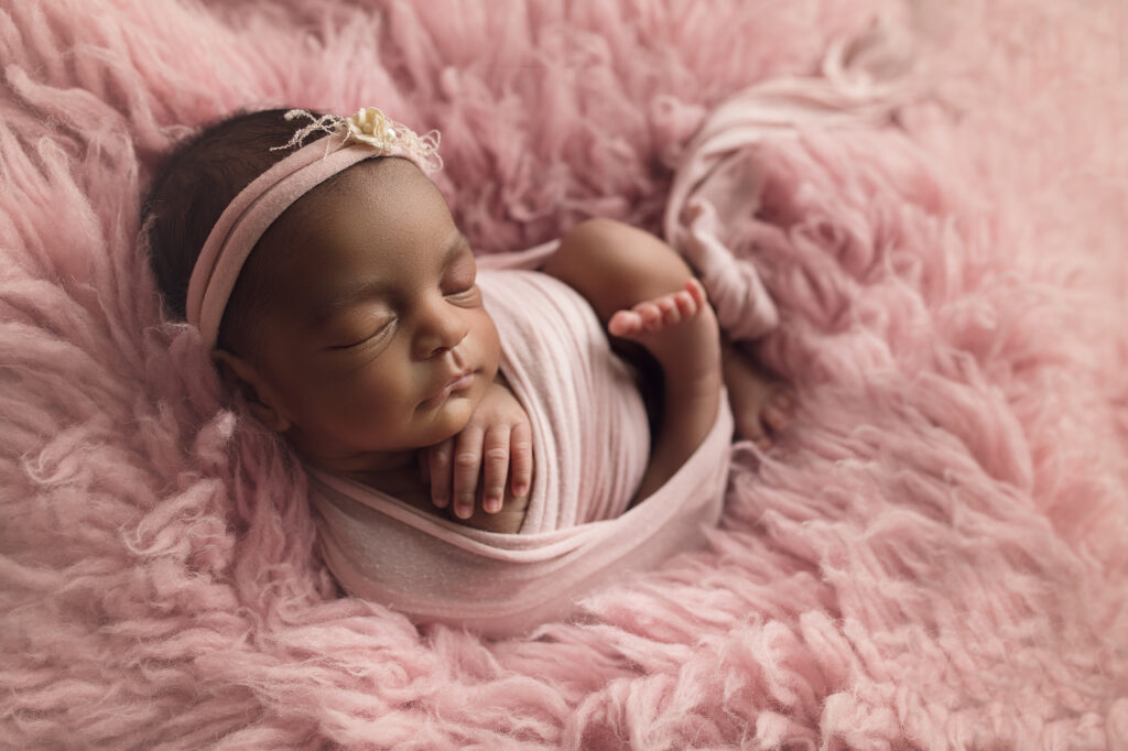 newborn triplet girl laying wrapped up in pink fur