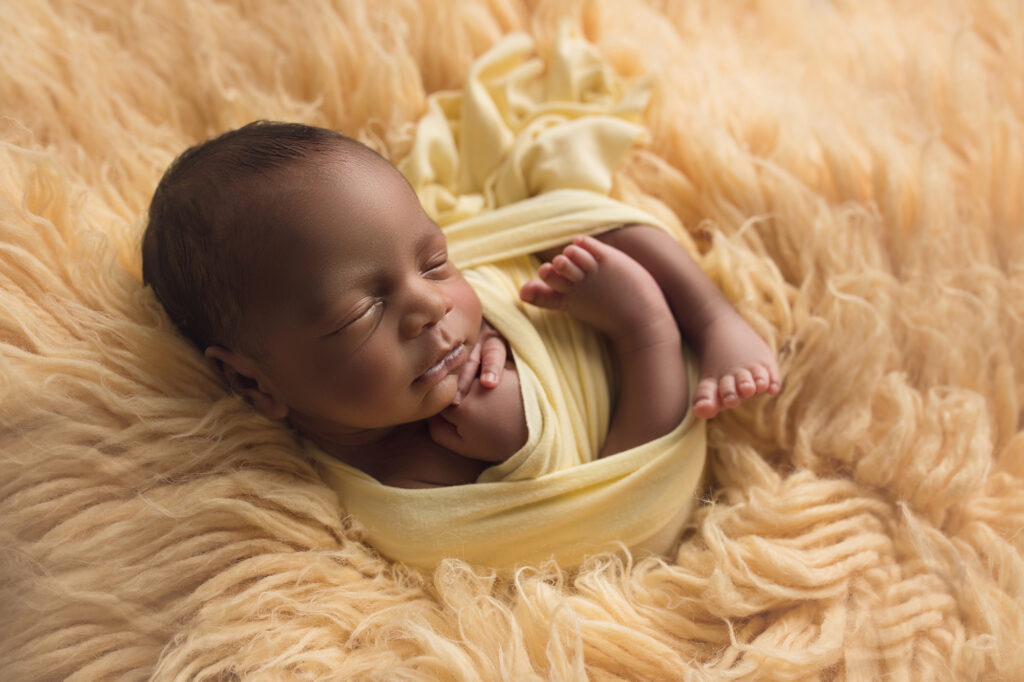 newborn triplet boy laying wrapped up in yellow fur