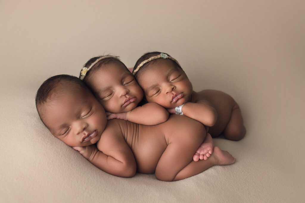 newborn triplet babies laying together on a beige blanket