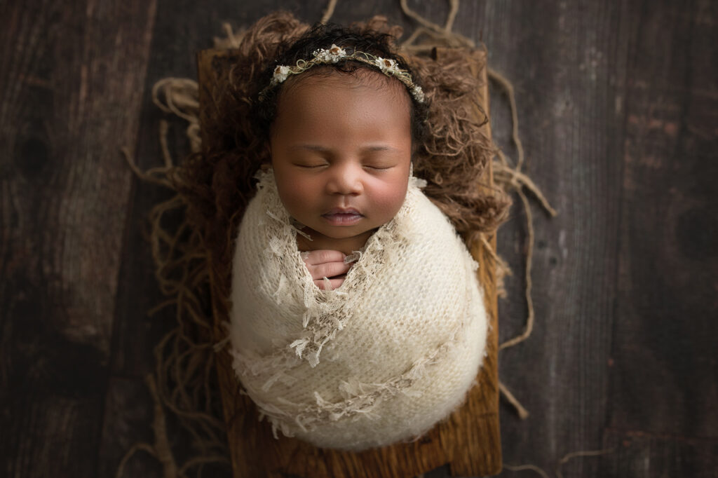 Newborn baby girl wrapped in beige wrap with floral headband