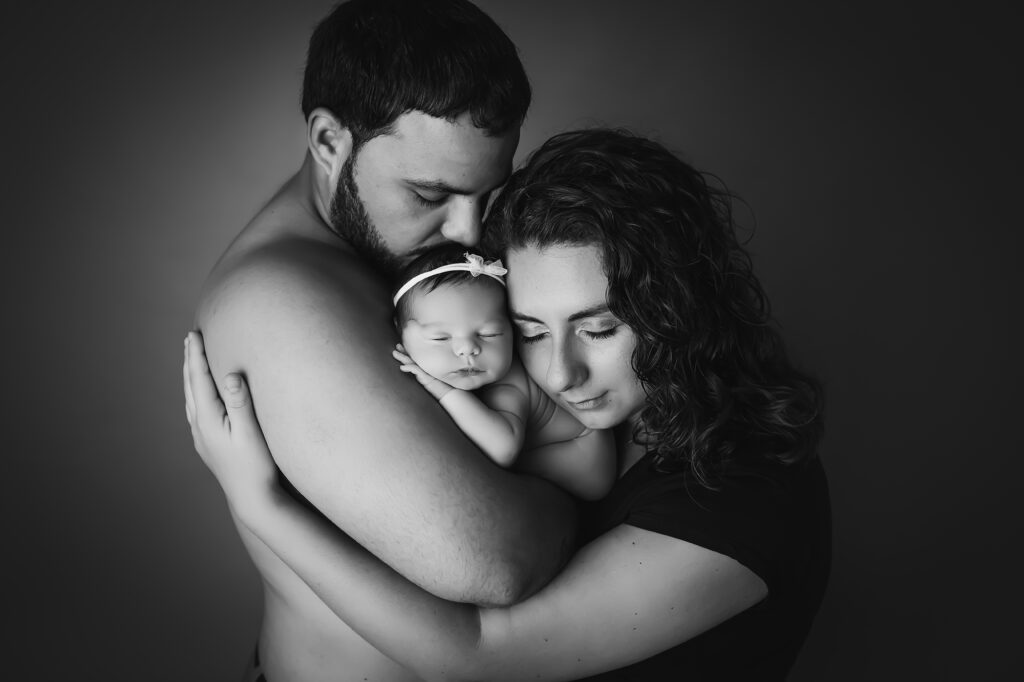 newborn baby girl in white wrapped being snuggled by parents black and white