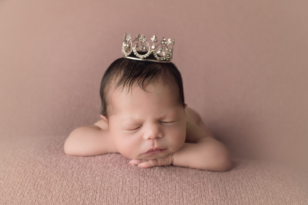 Newborn baby girl face forward on pink blanket wearing princess crown