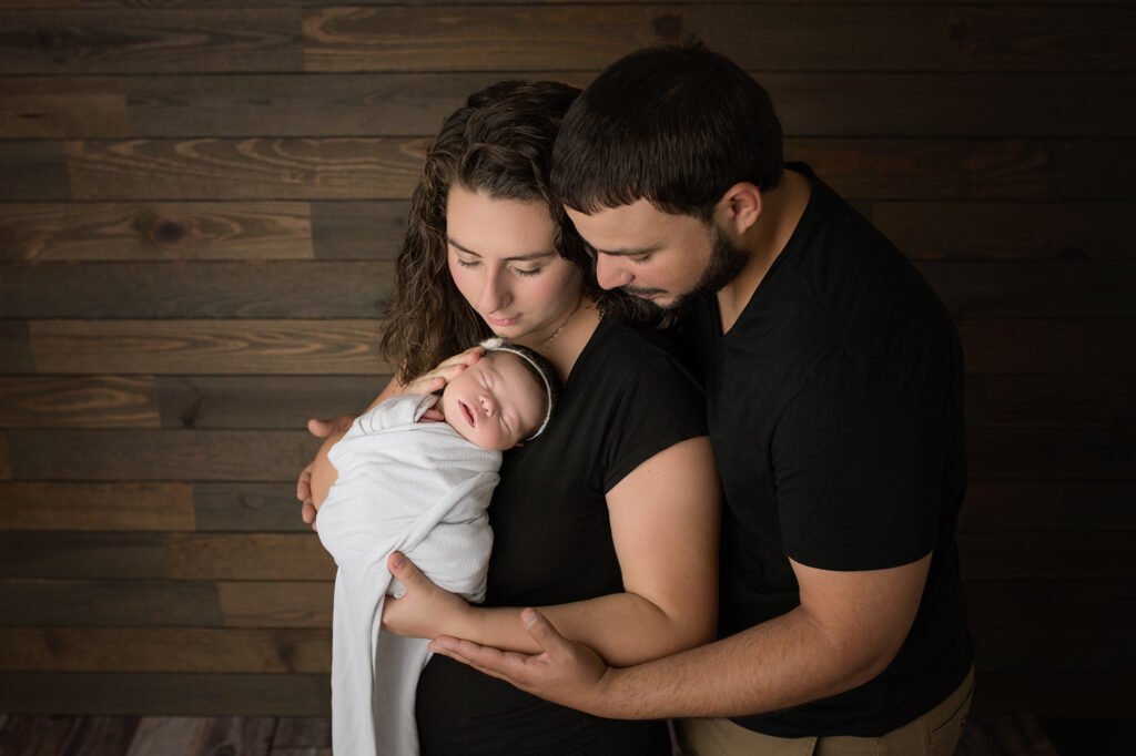 newborn baby girl in white wrapped being snuggled by parents