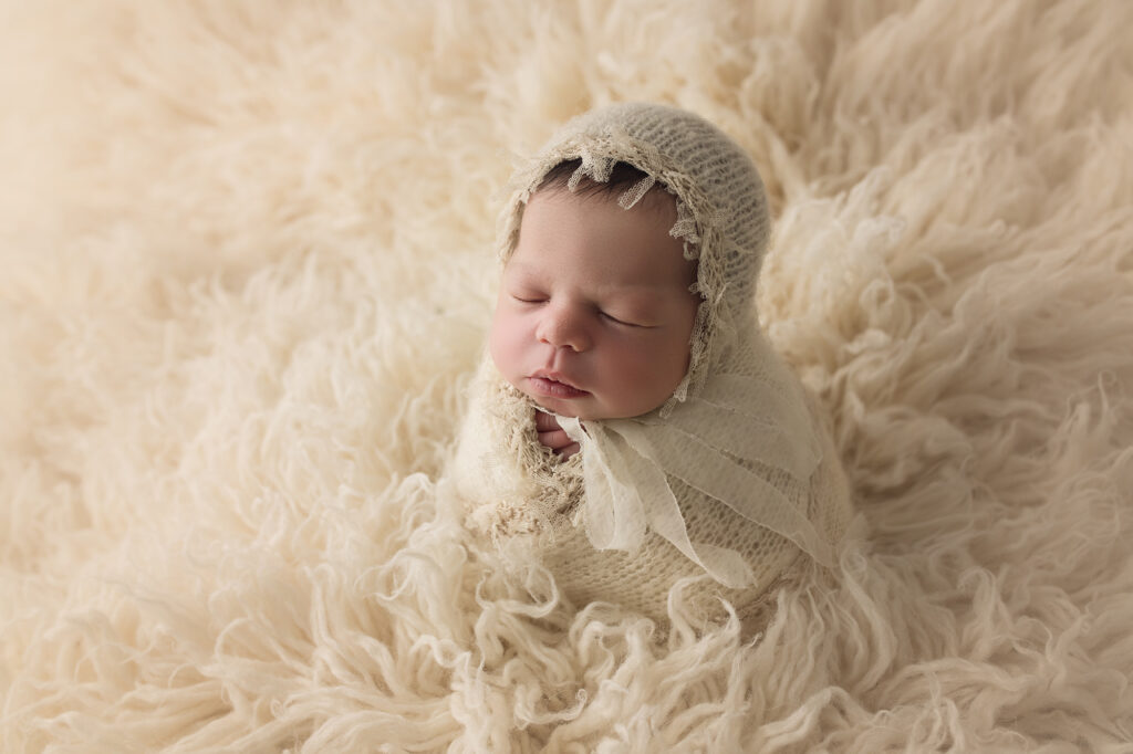newborn baby girl wrapped in cream wrap and matching bonnet in cream fur
