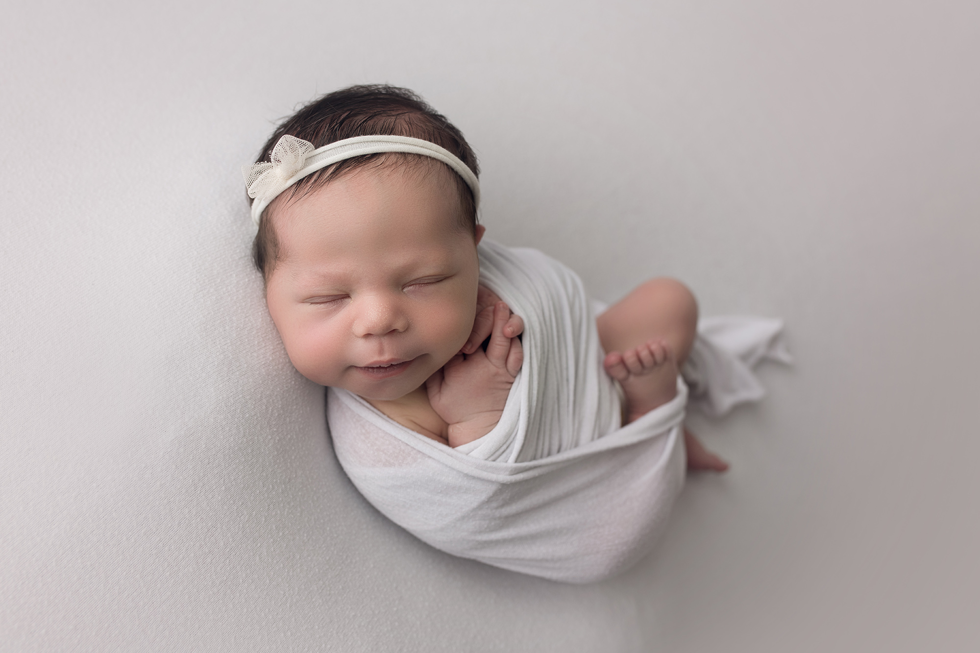 newborn baby girl wrapped in white wrap and white headband