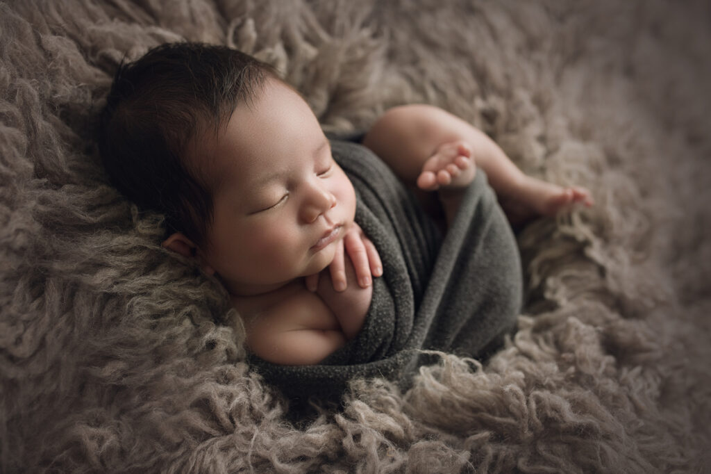 newborn baby boy wrapped in gray on gray fur