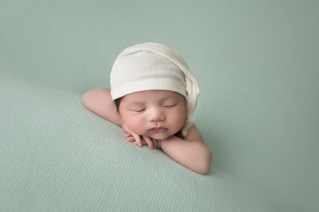 Newborn baby boy laying on hands with white sleepy cap
