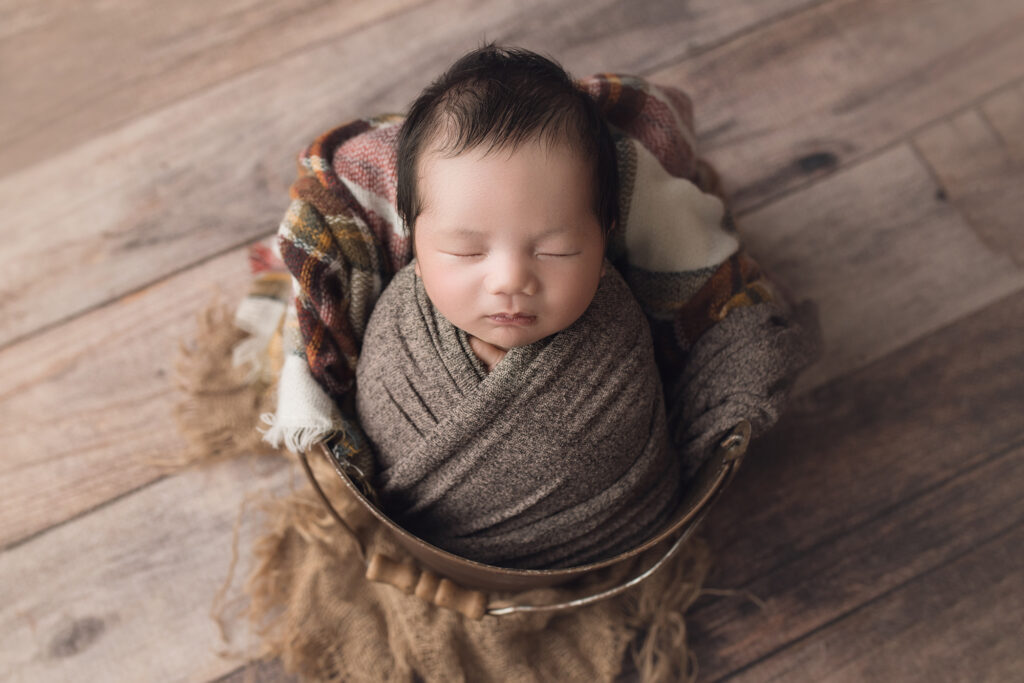 newborn baby boy in pail on brown plaid blanket